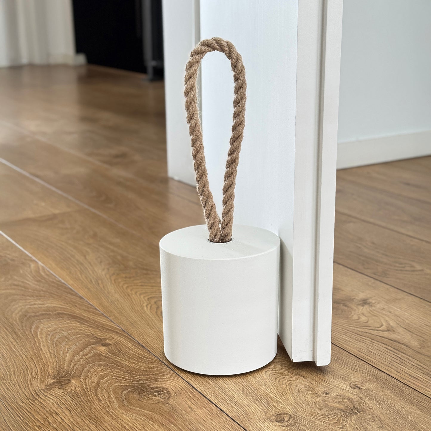Front view of an extra-large white concrete door stopper with a cylindrical shape and jute handle, placed against a door in a neutral modern interior. Sleek and minimalist, ideal for contemporary spaces and suitable for outdoor use.