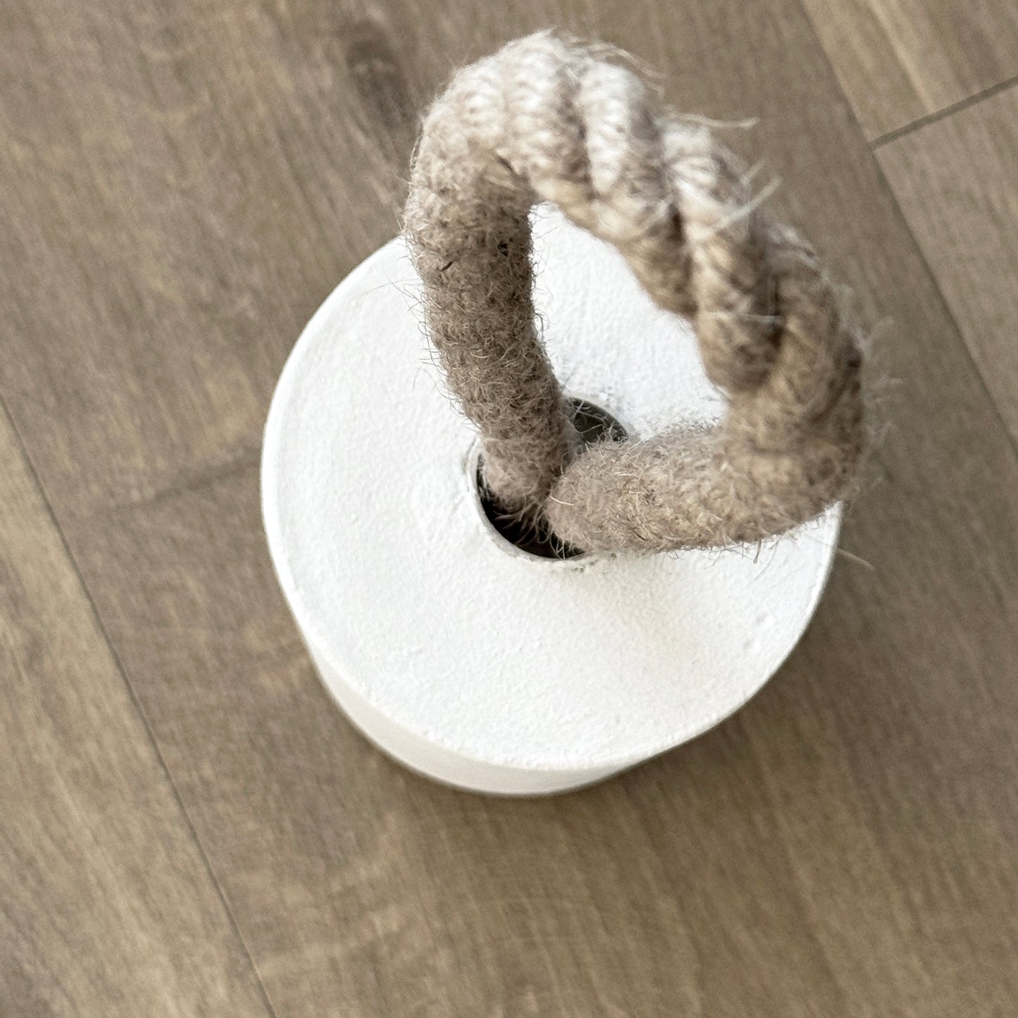 Top-down close-up of a concrete door stop in white, featuring a natural jute handle secured with a metal ring. Positioned next to a door, the image highlights the handle detail and showcases a clean, modern aesthetic.