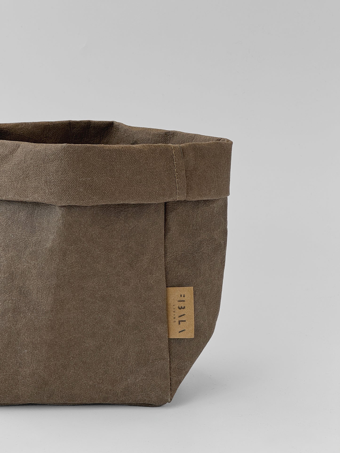 A close-up of a brown washable paper storage basket with a small tan brand tag reading 'Fibala Living' on a light gray background.