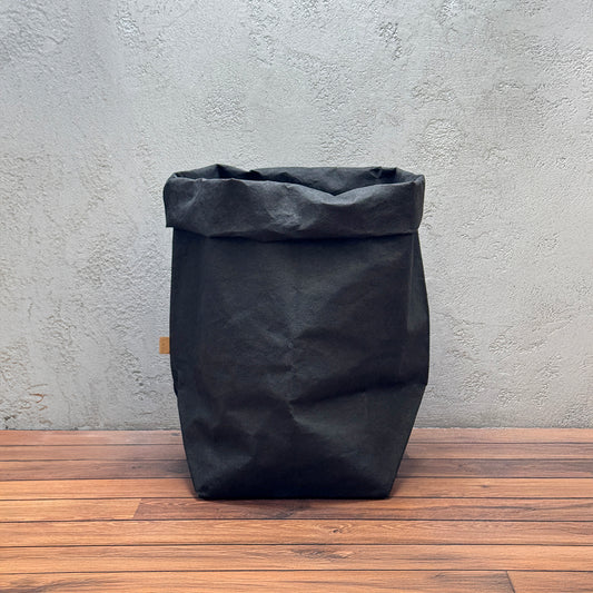 Black washable paper bag on a wooden surface with a gray textured wall background