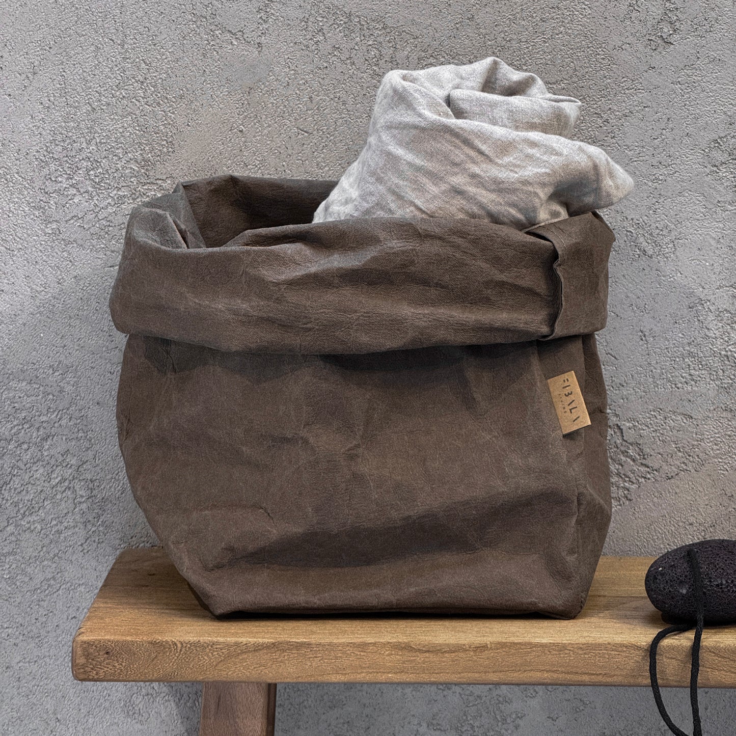 Extra-large cocoa brown washable paper bag, rolled to fit contents, with label, on wooden surface, gray wall background | Reusable eco-friendly bag