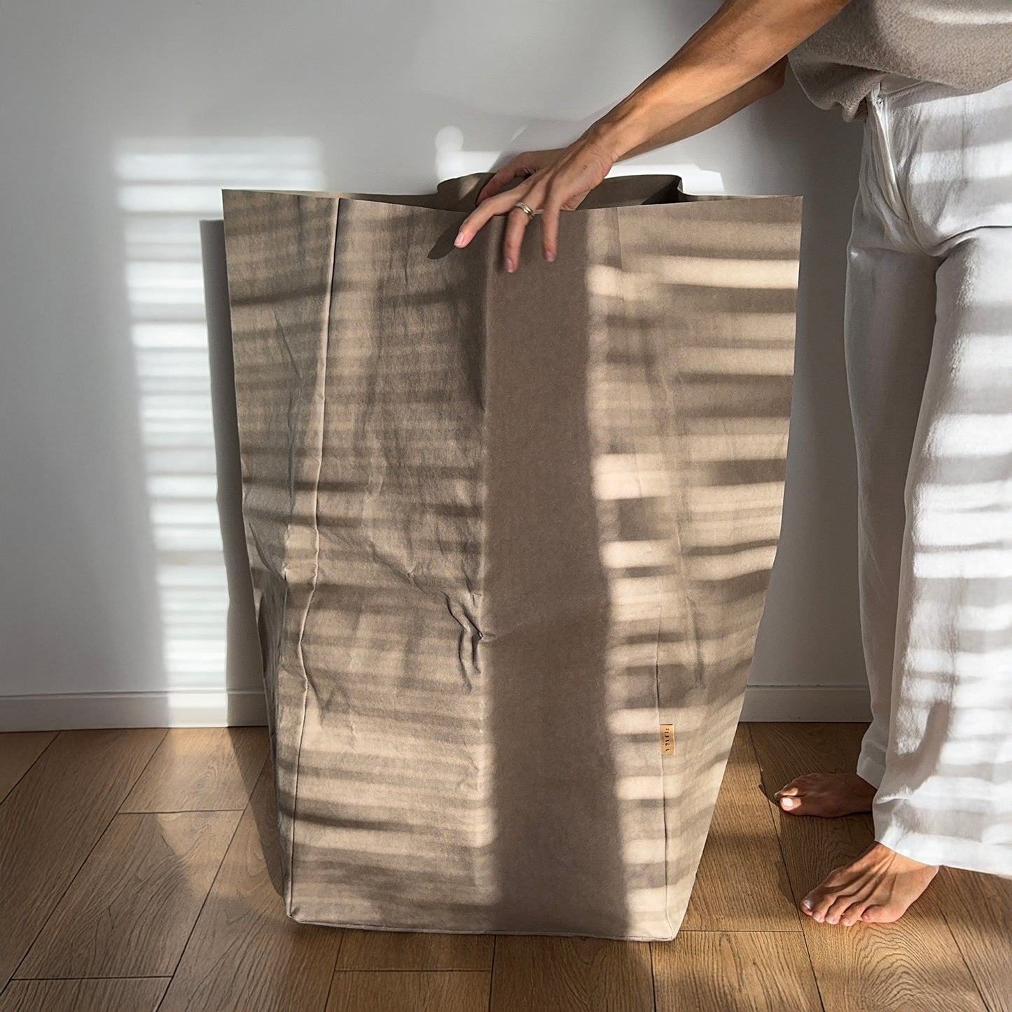 Person holding a giant washable paper bag, standing in a room with wooden flooring and white walls.