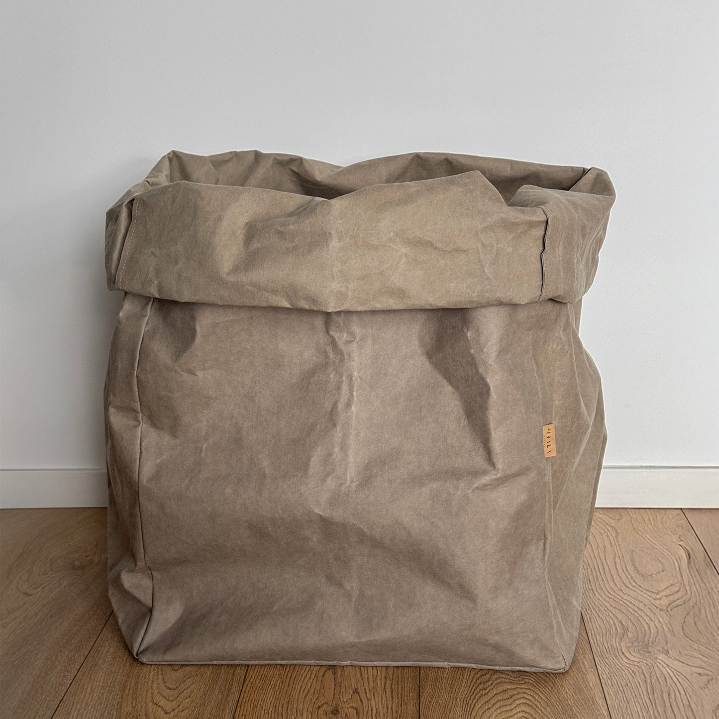 Giant chino washable paper bag on a wooden floor with a white wall background