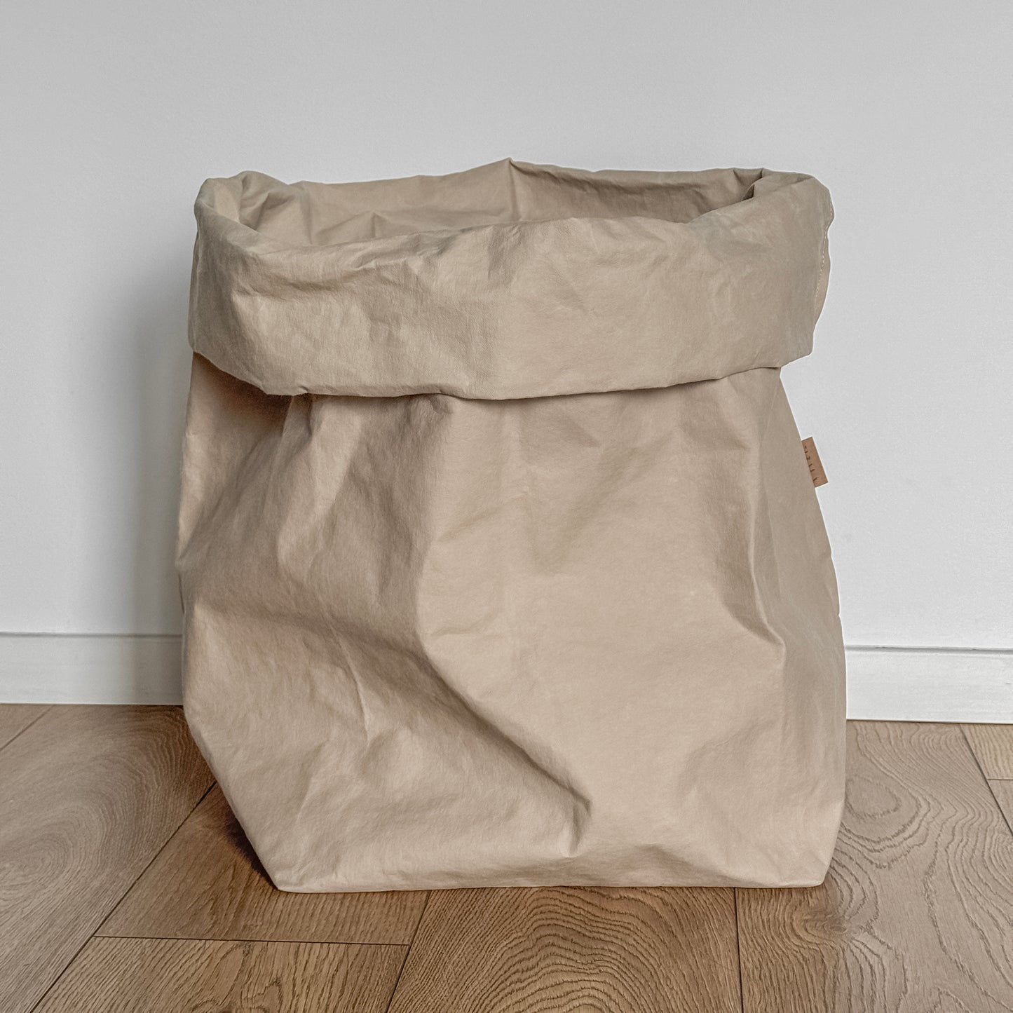 Sand beige washable paper bag on a wooden floor with a white wall background