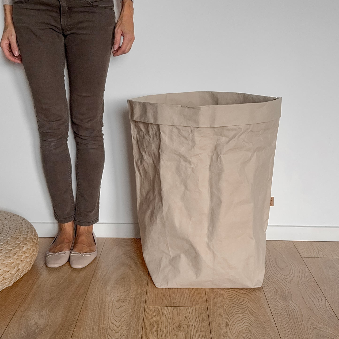Person standing next to a large beige washable paper bag on a wooden floor.