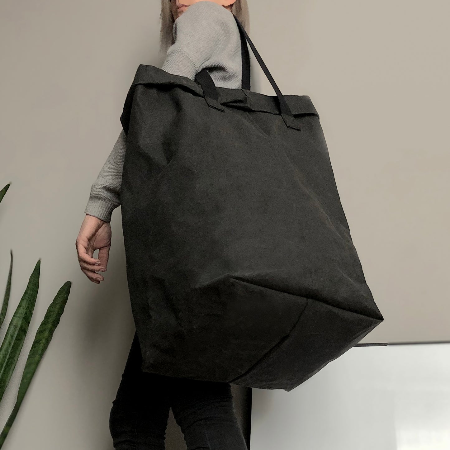 Person holding a large washable paper black laundry bag against a neutral background