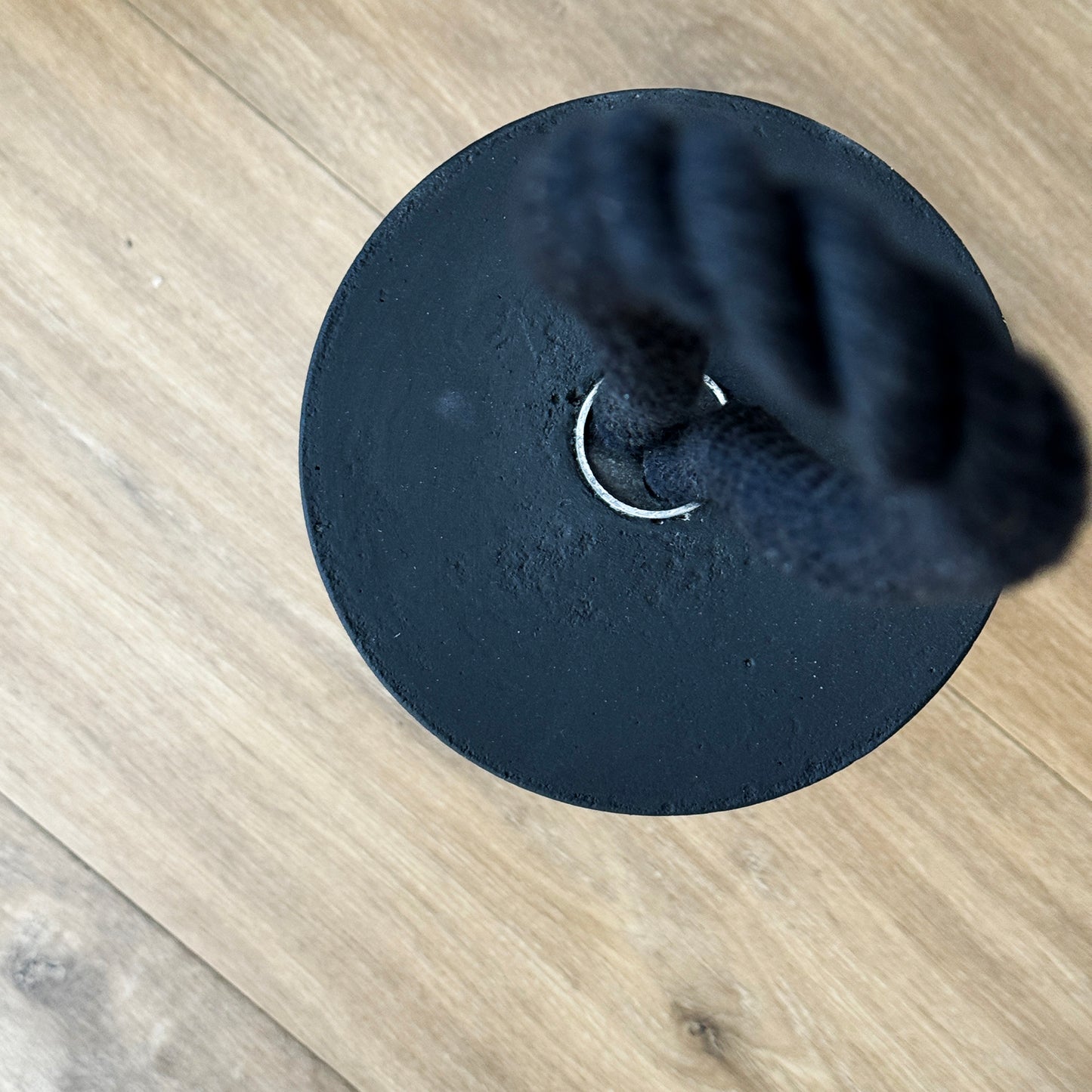 Top-down view of an extra large black concrete door stop, showcasing its smooth cylindrical shape and solid concrete base. The black cotton rope handle appears slightly blurred in the background, keeping focus on the raw texture and clean lines of the concrete. A sleek, functional accent for modern minimalist interiors and exteriors.