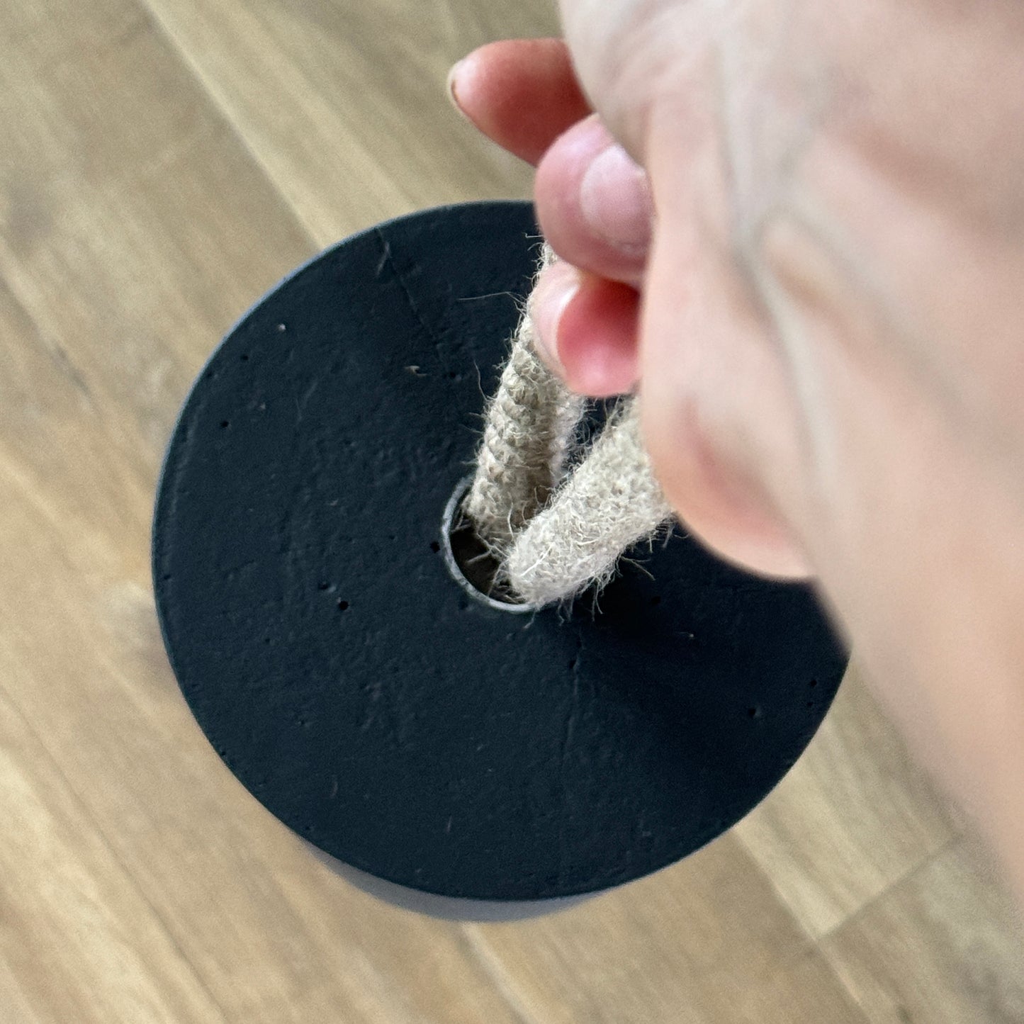 Top-down view of an extra large black concrete door stop, showcasing its smooth cylindrical shape and solid concrete base. The black cotton rope handle appears slightly blurred in the background, keeping focus on the raw texture and clean lines of the concrete. A sleek, functional accent for modern minimalist interiors and exteriors.