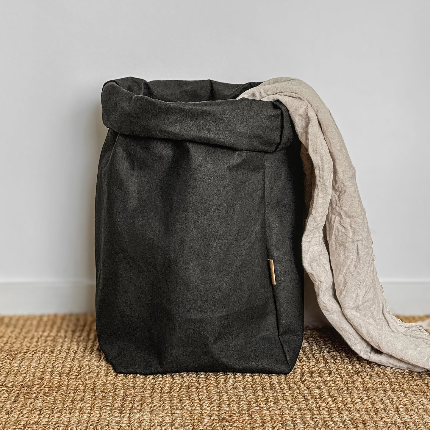 XXL Black washable paper bag with linen throw inside, on jute carpet, white background | Eco-friendly, versatile storage solution