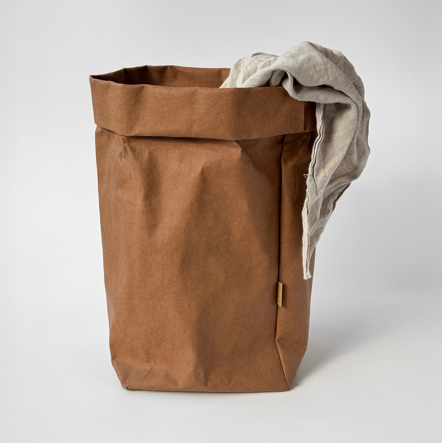 Close-up of XXL brown washable paper bag on light gray background, with linen throw fabric inside | Eco-friendly, versatile storage solution