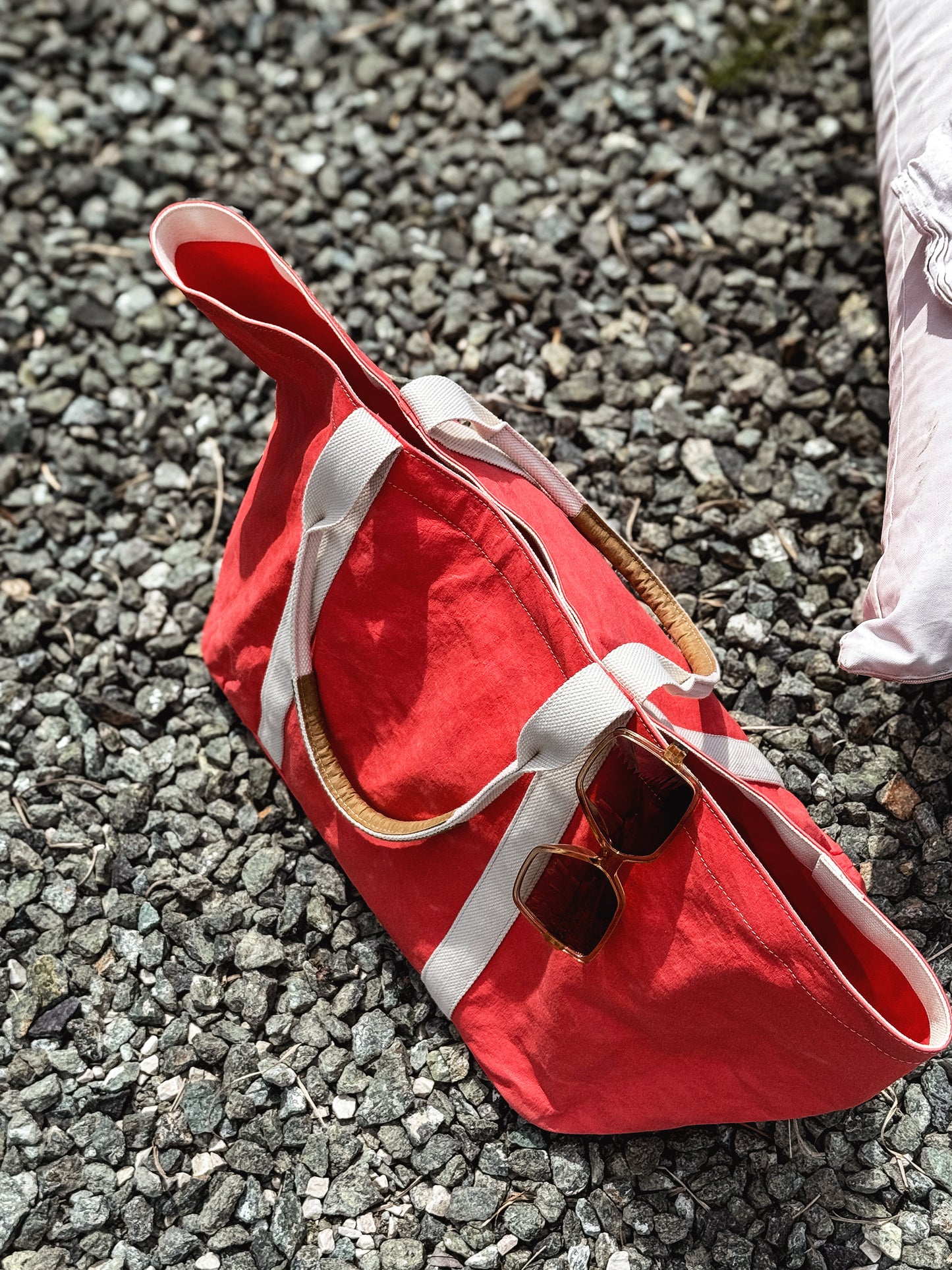 Large coral washable paper tote bag lying on gravel, sunglasses tucked into the side
