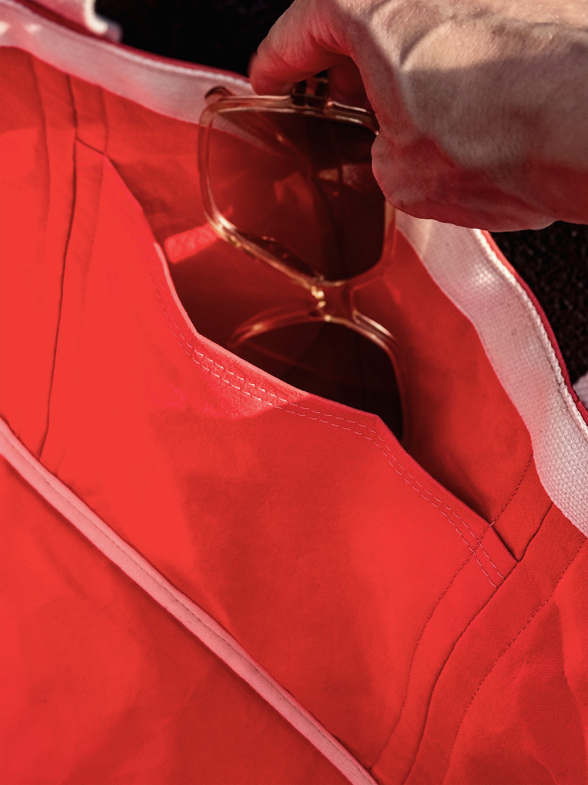 Close-up of the open side pocket on a coral washable paper tote bag, sunglasses sliding in