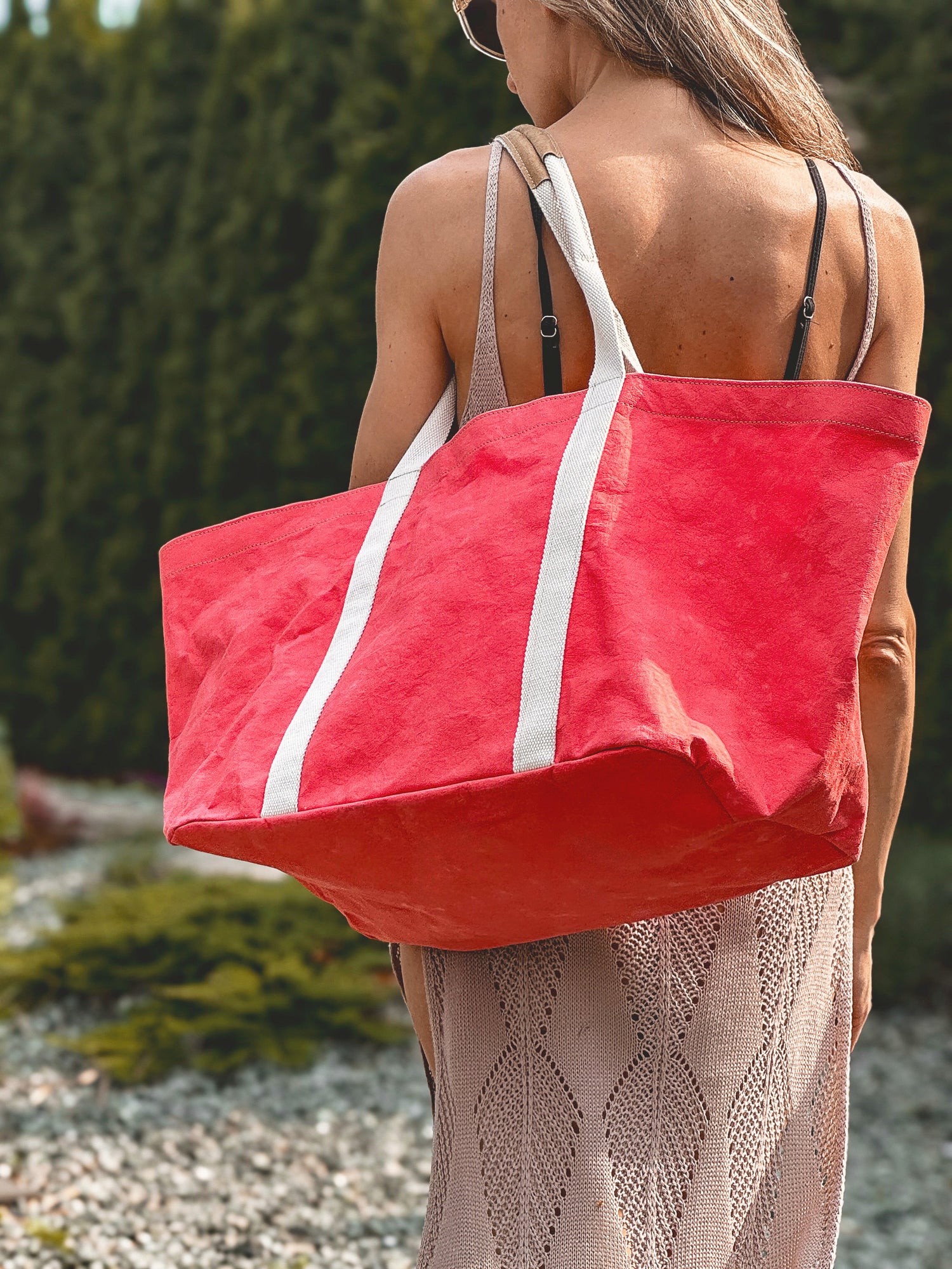 Large coral washable paper tote bag on shoulder, rear view showing full bag volume and white cotton handles