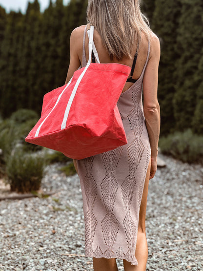 Large coral washable paper tote bag worn on the shoulder from behind, structured shape, garden background