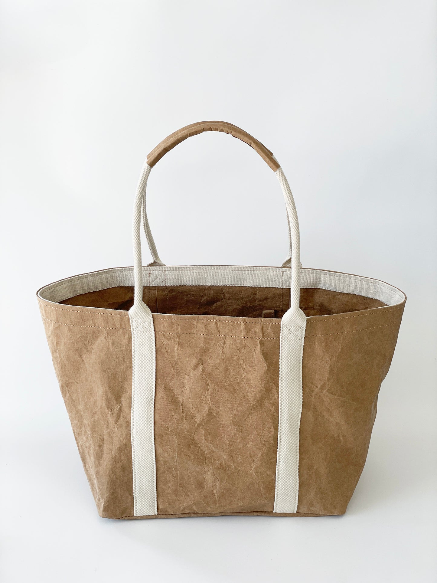 Brown washable paper tote bag product shot on white background, open top, white cotton handles with washable paper wrap detail