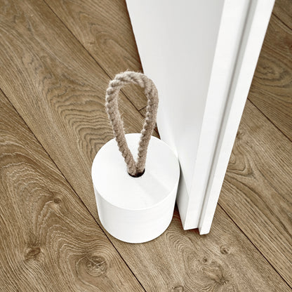 Top-down close-up of an extra-large white concrete door stopper with a cylindrical shape and natural jute handle, positioned against an open interior door in a neutral modern interior. Designed to keep the door open.