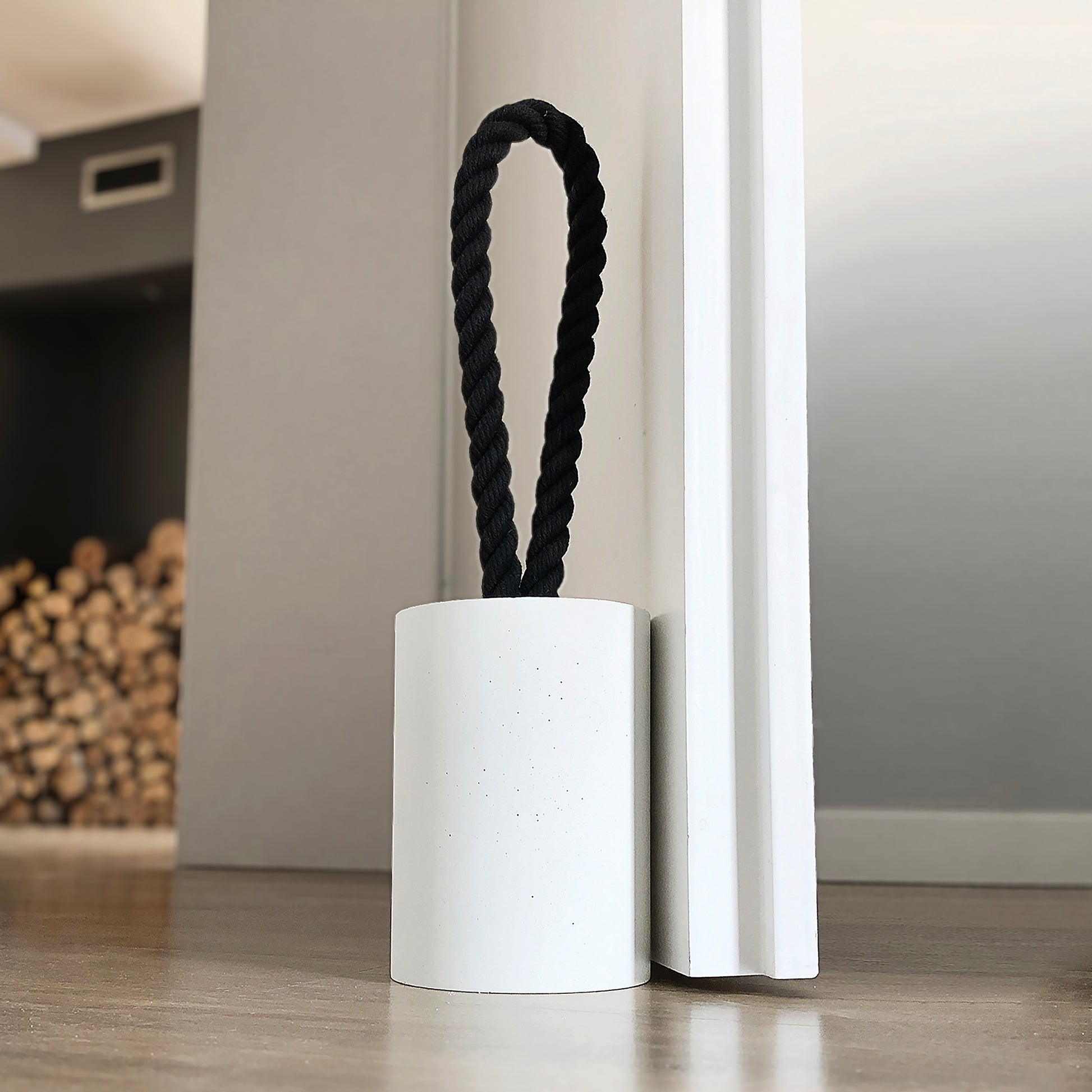 Close-up, top-down view of white concrete door stop with a loop-style black cotton rope handle. The image highlights the raw, textured concrete surface and the twisted rope detail, showcasing its sturdy build and minimalist design. A functional, stylish piece for modern interiors and exteriors.