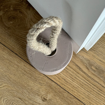 Top-down close-up of a concrete door stop in earthy Desert Taupe Brown, featuring a natural jute handle secured with a metal ring. Positioned next to a door, the image highlights the handle detail and showcases a clean, modern aesthetic.