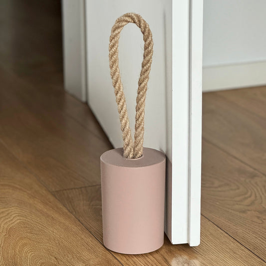 Front view of a concrete door stop with a natural jute handle in earthy Desert Taupe Brown, placed next to an open white door in a modern interior. The focus is on the door stop and the lower part of the door, with the background softly blurred to highlight the product.