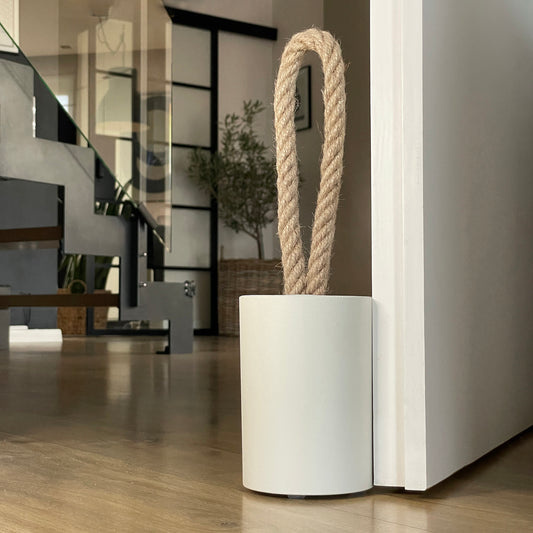 Concrete door stop with a natural jute handle in earthy Linen White, positioned next to an open door. The close-up highlights the textured concrete surface, with a modern, earthy-toned interior in the background. A perfect accent for contemporary rustic, farmhouse, boho, coastal, or minimalist Scandinavian-style interiors.