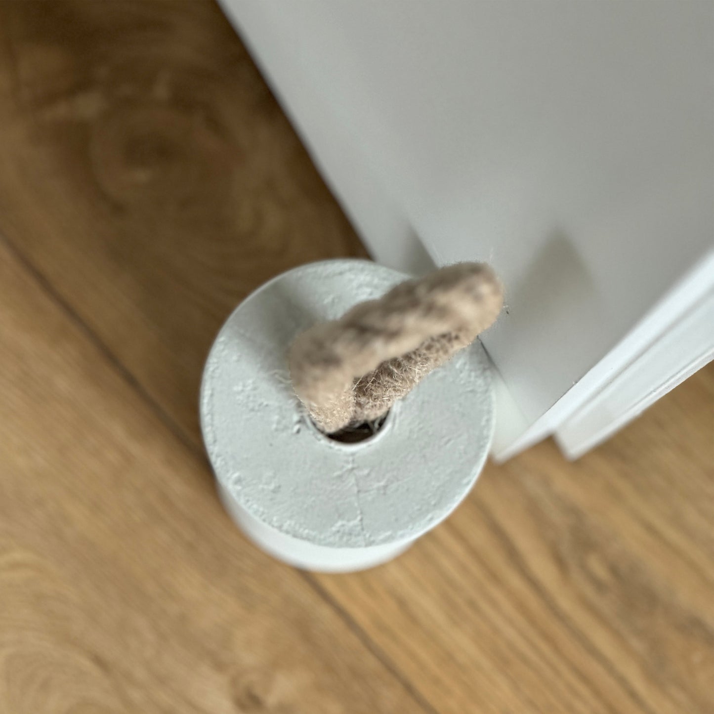 Top-down close-up of a concrete door stop in earthy Linen White, featuring a natural jute handle secured with a metal ring. Positioned next to a door, the image highlights the handle detail and showcases a clean, modern aesthetic.