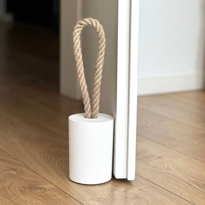 White, round concrete door stop with a natural jute handle, positioned against a door in a neutral modern interior. A sleek, minimalist design, perfect for contemporary door stops in modern spaces.