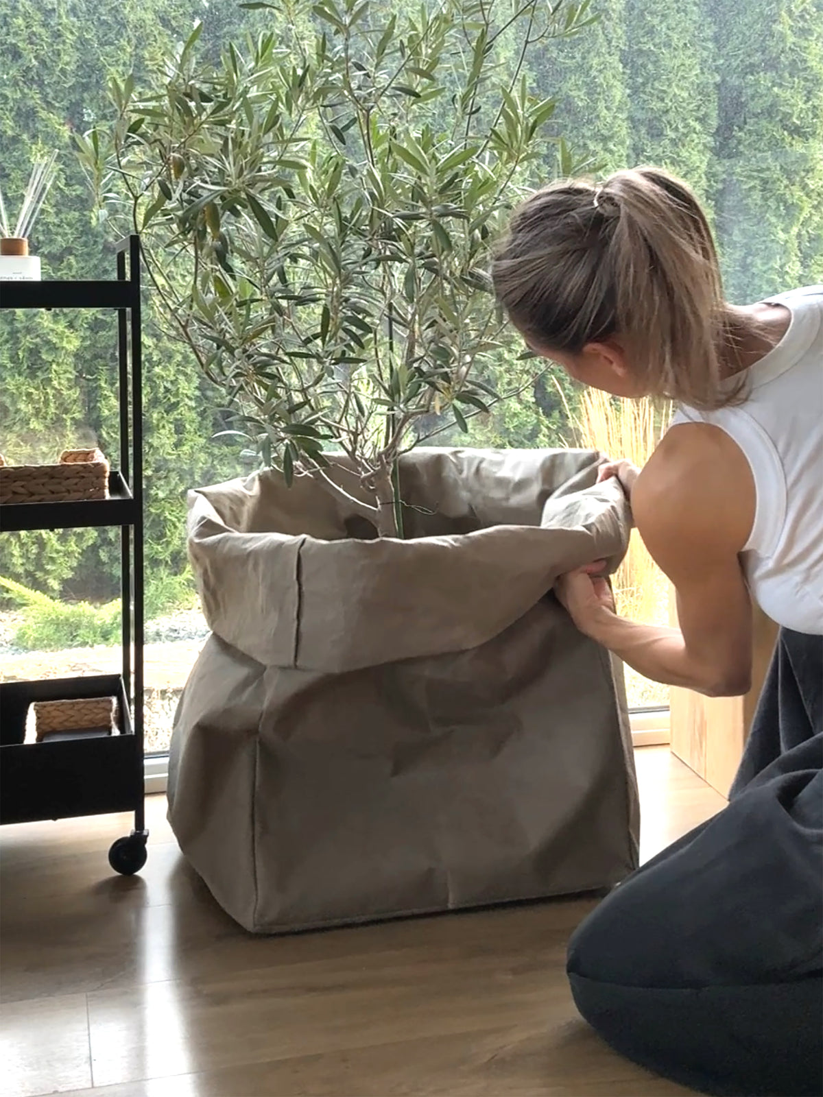 Woman rolling down the top of a large washable paper storage bag with a leafy plant, chino color, styling tutorial