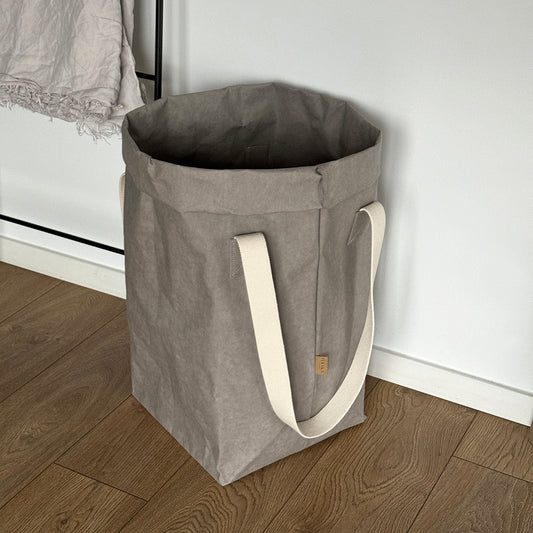 Gray washable paper laundry basket, long cotton handles, side view on wood floor, eco storage