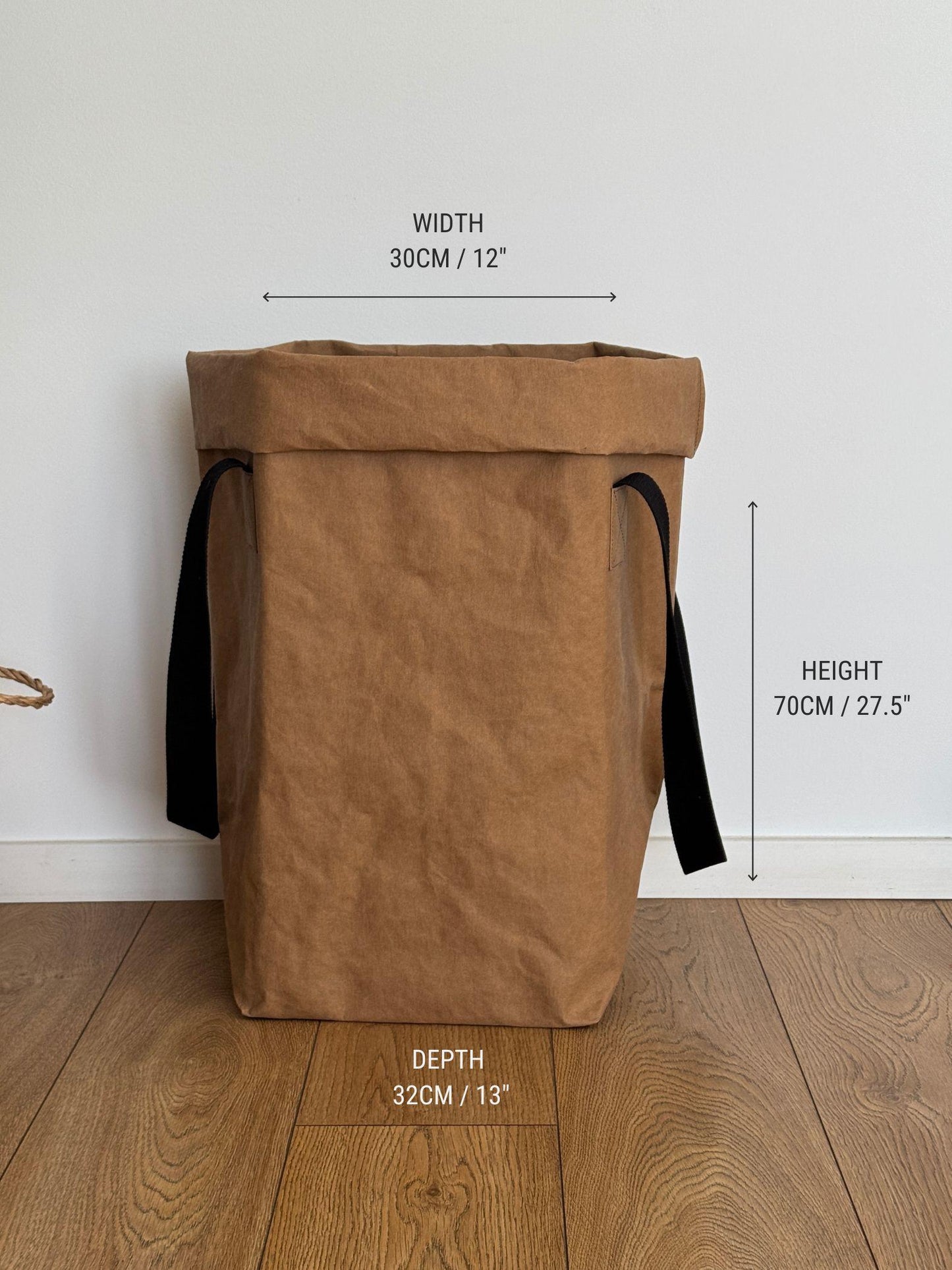 A brown washable paper storage bin with black side handles, shown on a wood floor against a white wall with overlaid dimension labels for width, height, and depth.