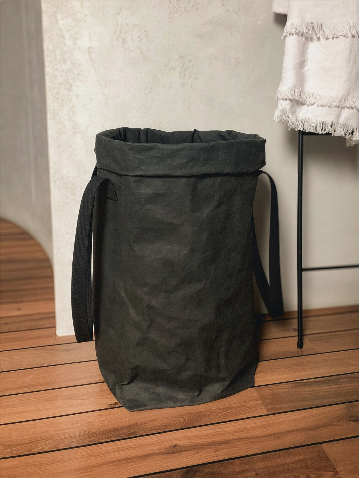 Black washable paper laundry basket with black cotton handles beside a towel rack