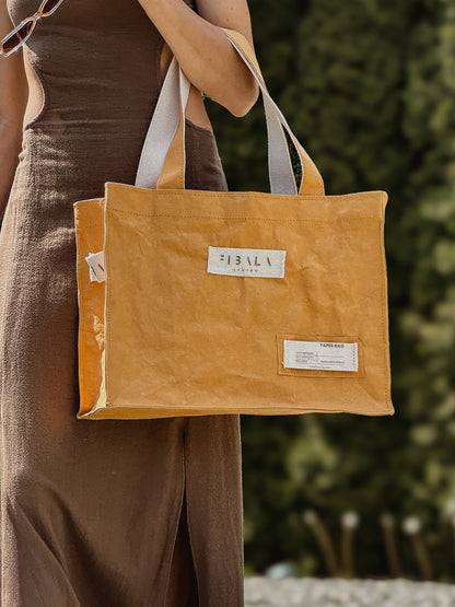 Mustard yellow washable paper carry-all bag held against a green background — Fibala Living L size