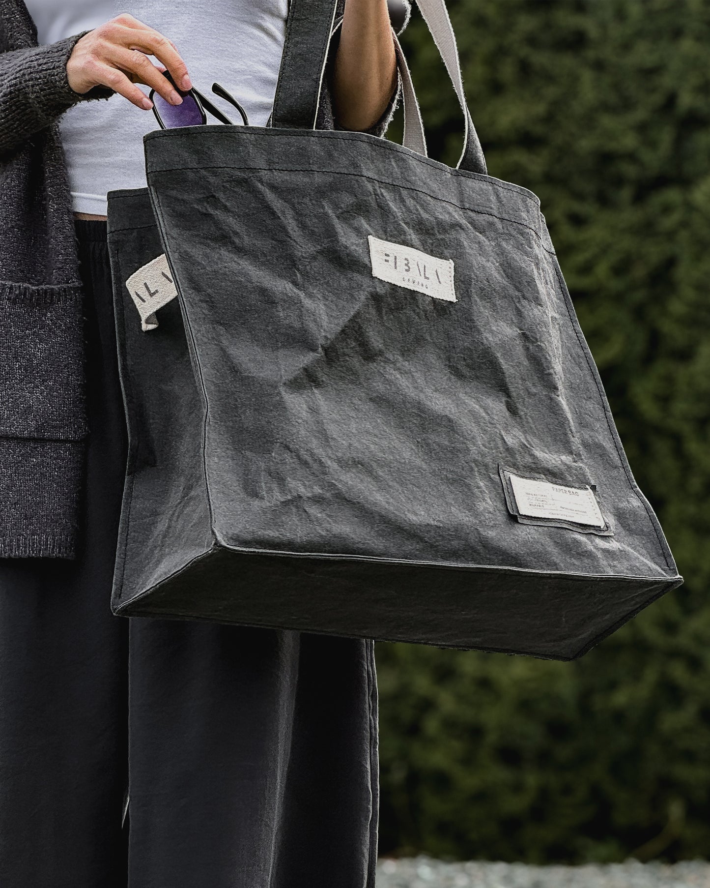Sunglasses being placed into the cotton logo patch on a black Fibala carry-all bag — XL size