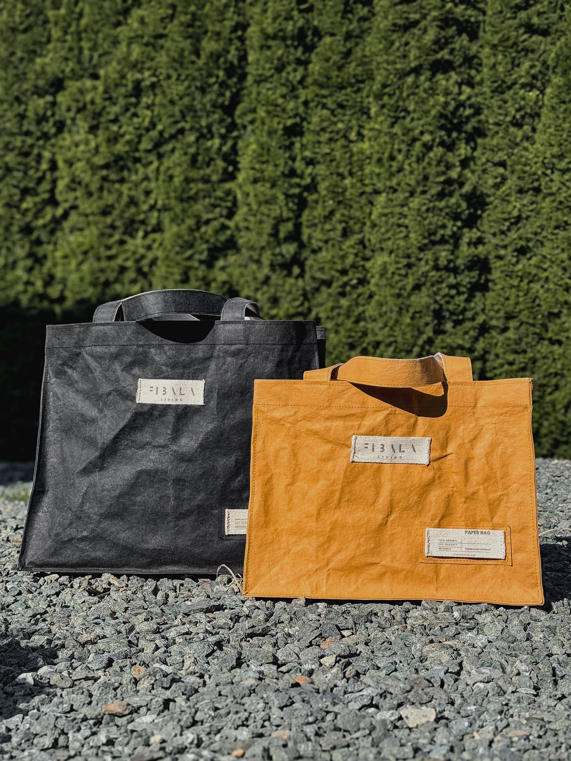 Fibala carry-all bags in black and mustard yellow on gravel — L and XL size comparison