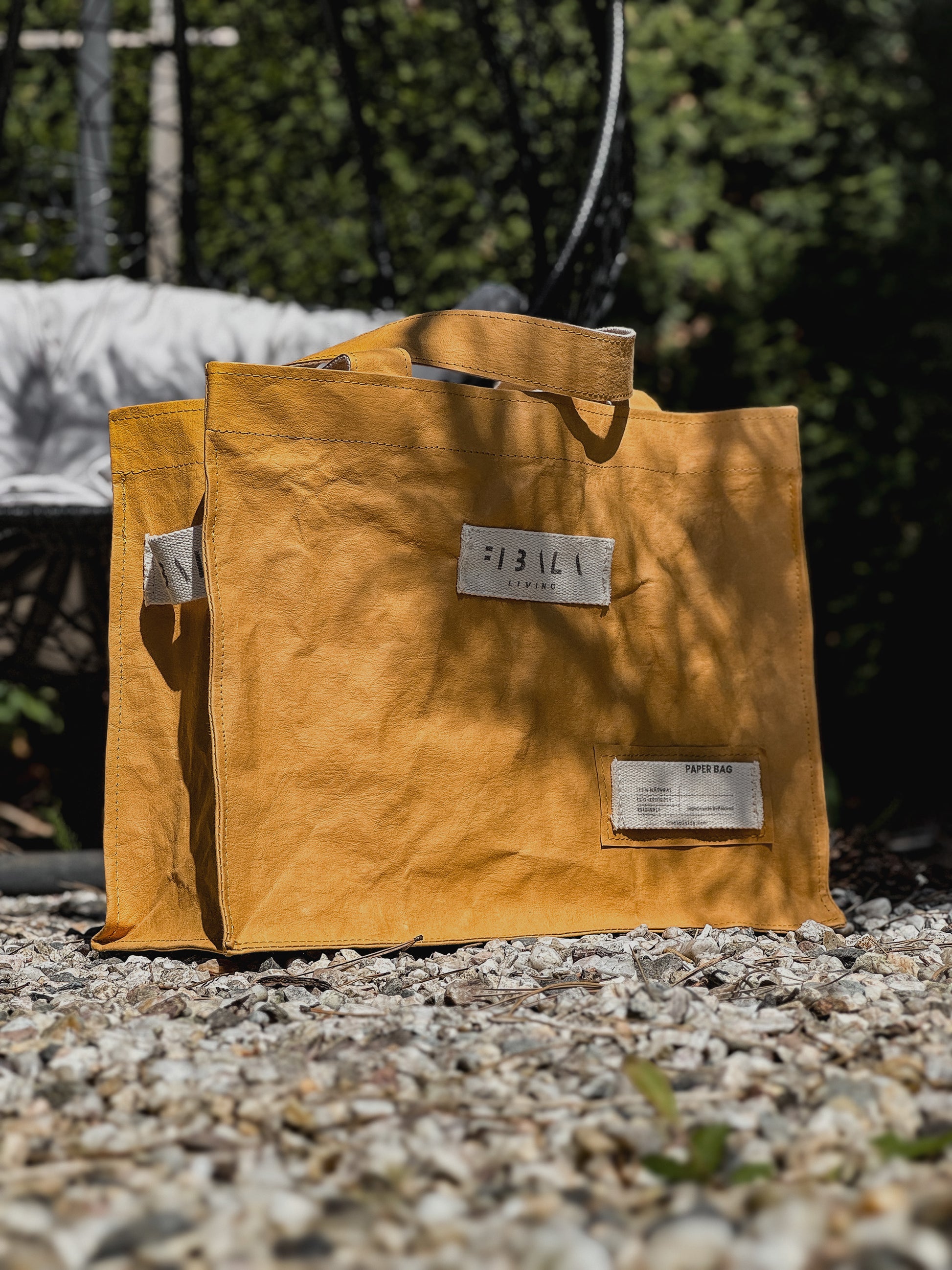 Mustard yellow Fibala carry-all bag on gravel, angled view showing cotton logo side patch — L size