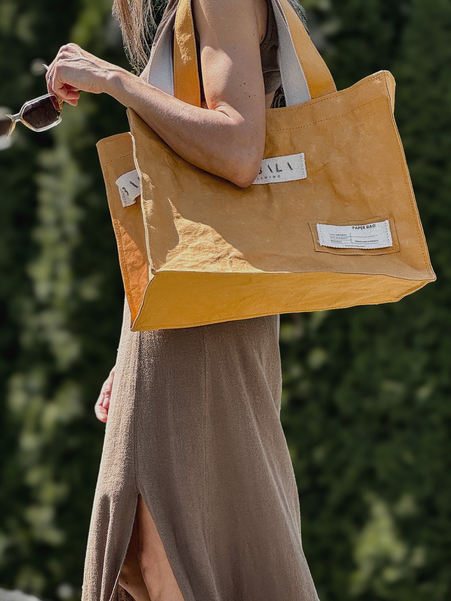 Mustard yellow washable paper carry-all bag, side view, held against green background — Fibala Living L size