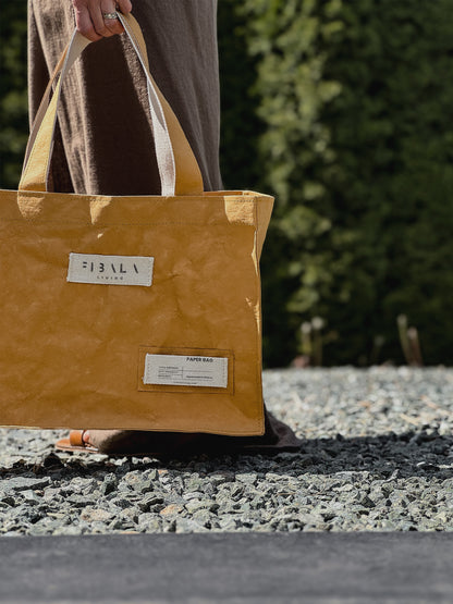 Mustard yellow Fibala carry-all bag carried along a gravel path with garden greenery — L size