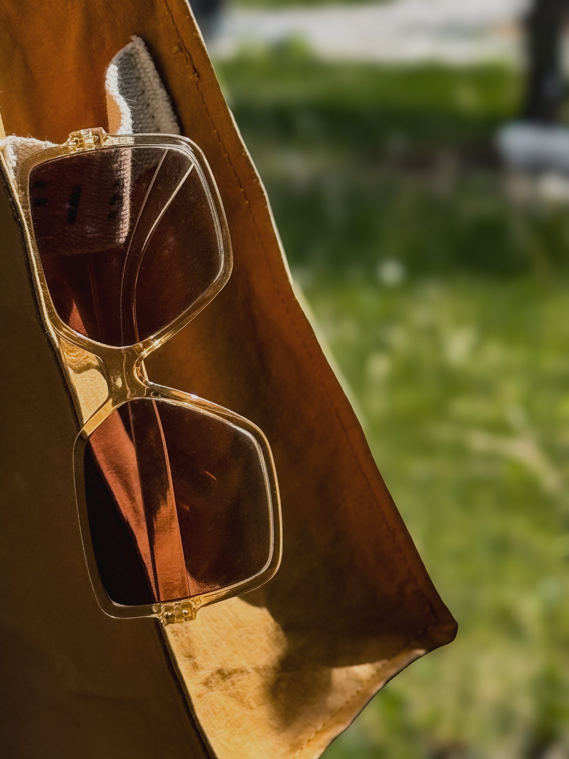 Sunglasses resting in the cotton logo patch on a mustard yellow Fibala carry-all bag — outdoor setting