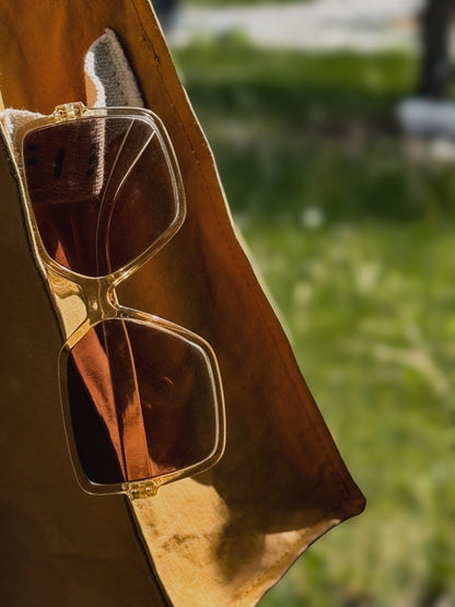 Sunglasses resting in the cotton logo patch on a mustard yellow Fibala carry-all bag — outdoor setting