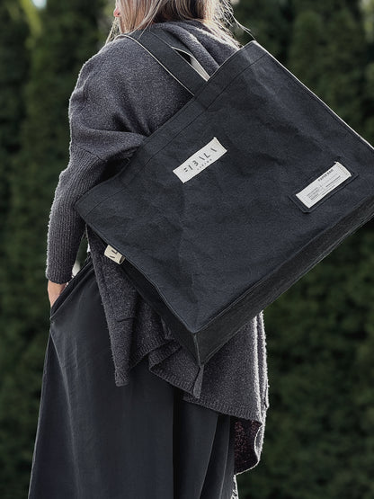 Black Fibala carry-all bag on shoulder, close-up side view showing cotton logo patch — XL size