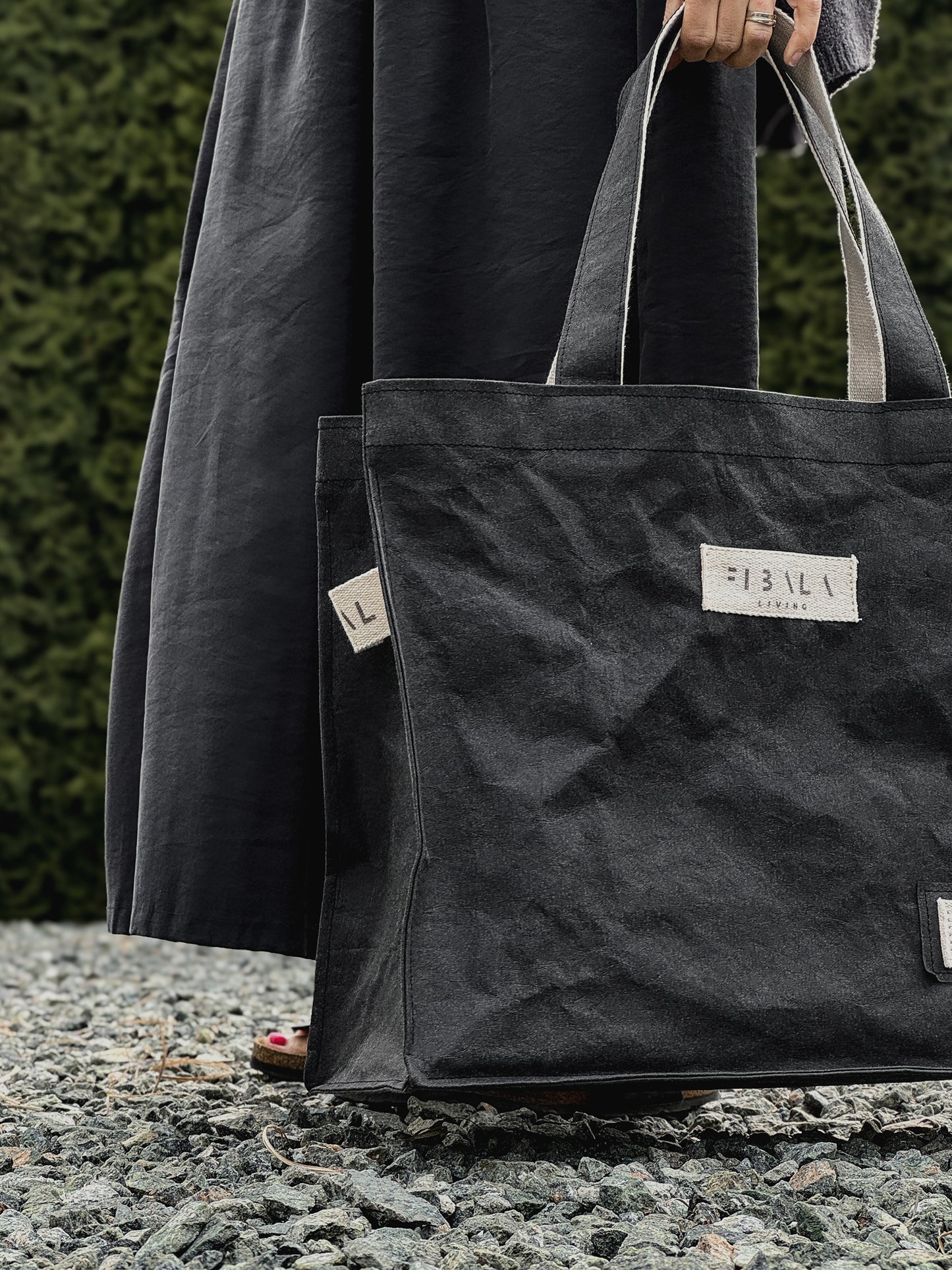 Black washable paper carry-all bag with Fibala branding held against a green hedge — XL size