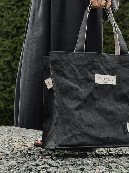 Black washable paper carry-all bag with Fibala branding held against a green hedge — XL size