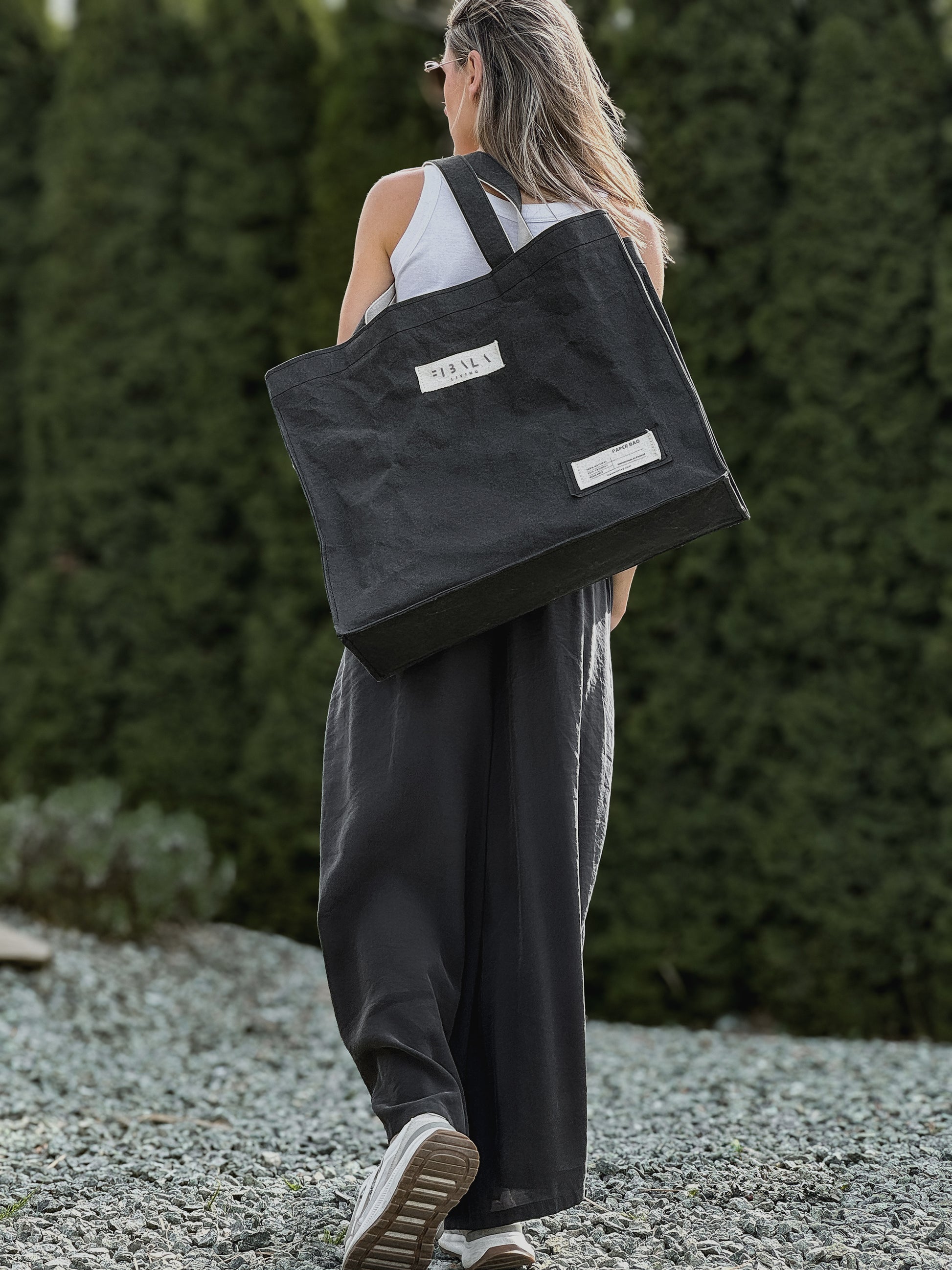 Black washable paper carry-all bag with Fibala branding held against a green hedge — XL size
