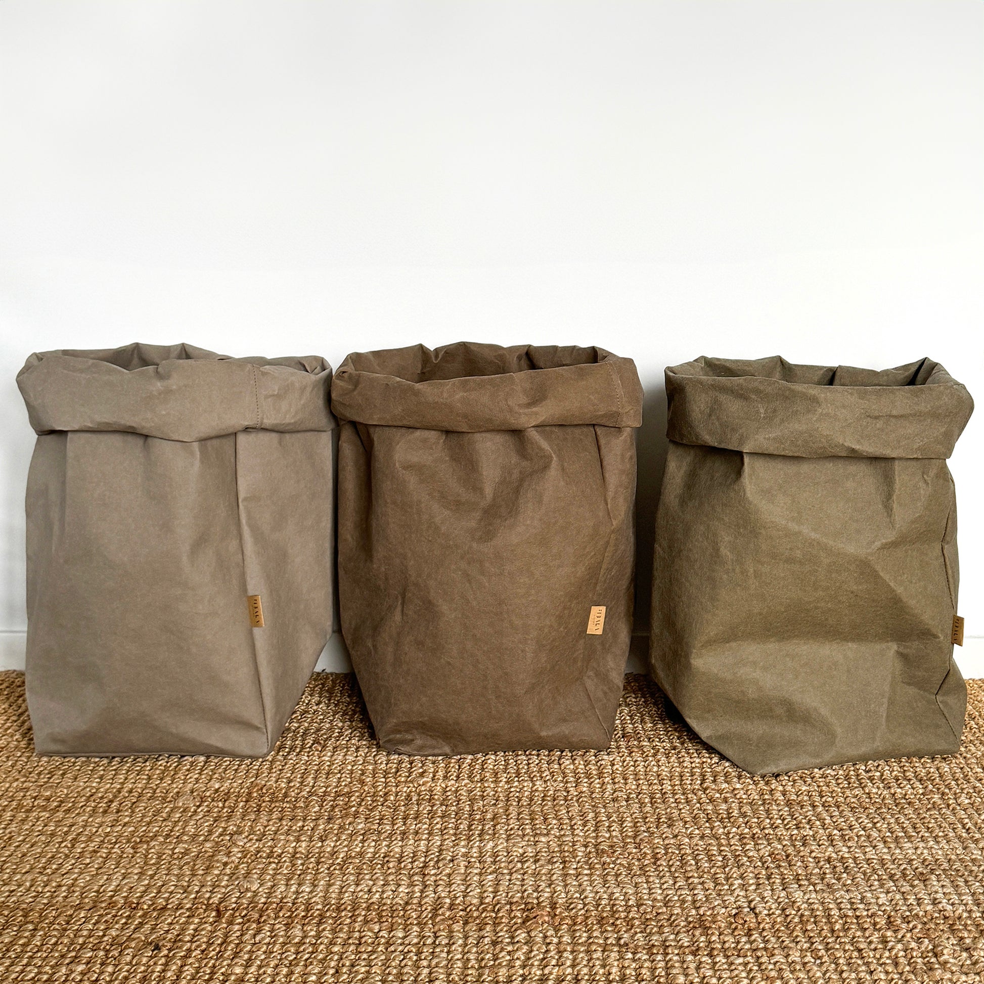 Three brown extra large washable paper bags on a textured surface with a white wall background.
