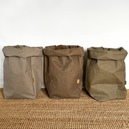 Three brown extra large washable paper bags on a textured surface with a white wall background.
