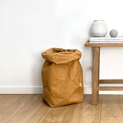 Brown washable paper bag on a wooden floor with a wooden side table and decorative items in the background.