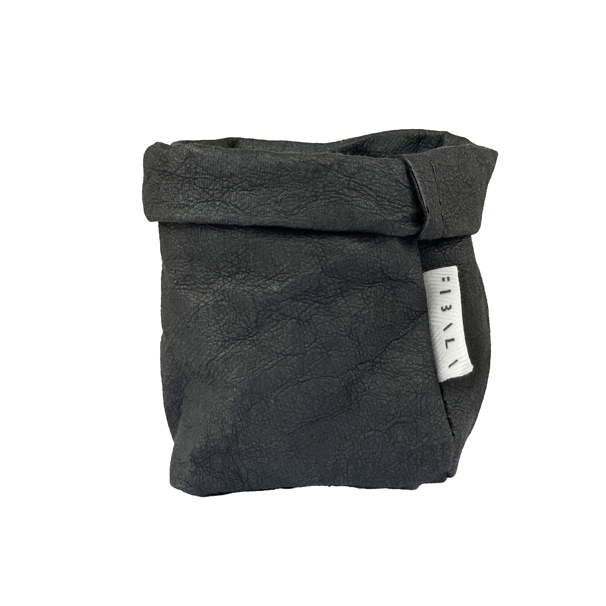 A small, aged kind of style black washable paper bag in size XS with a folded top. A white label with black logo is stitched on one side. The bag has a minimalist design , with a soft, textured appearance. 