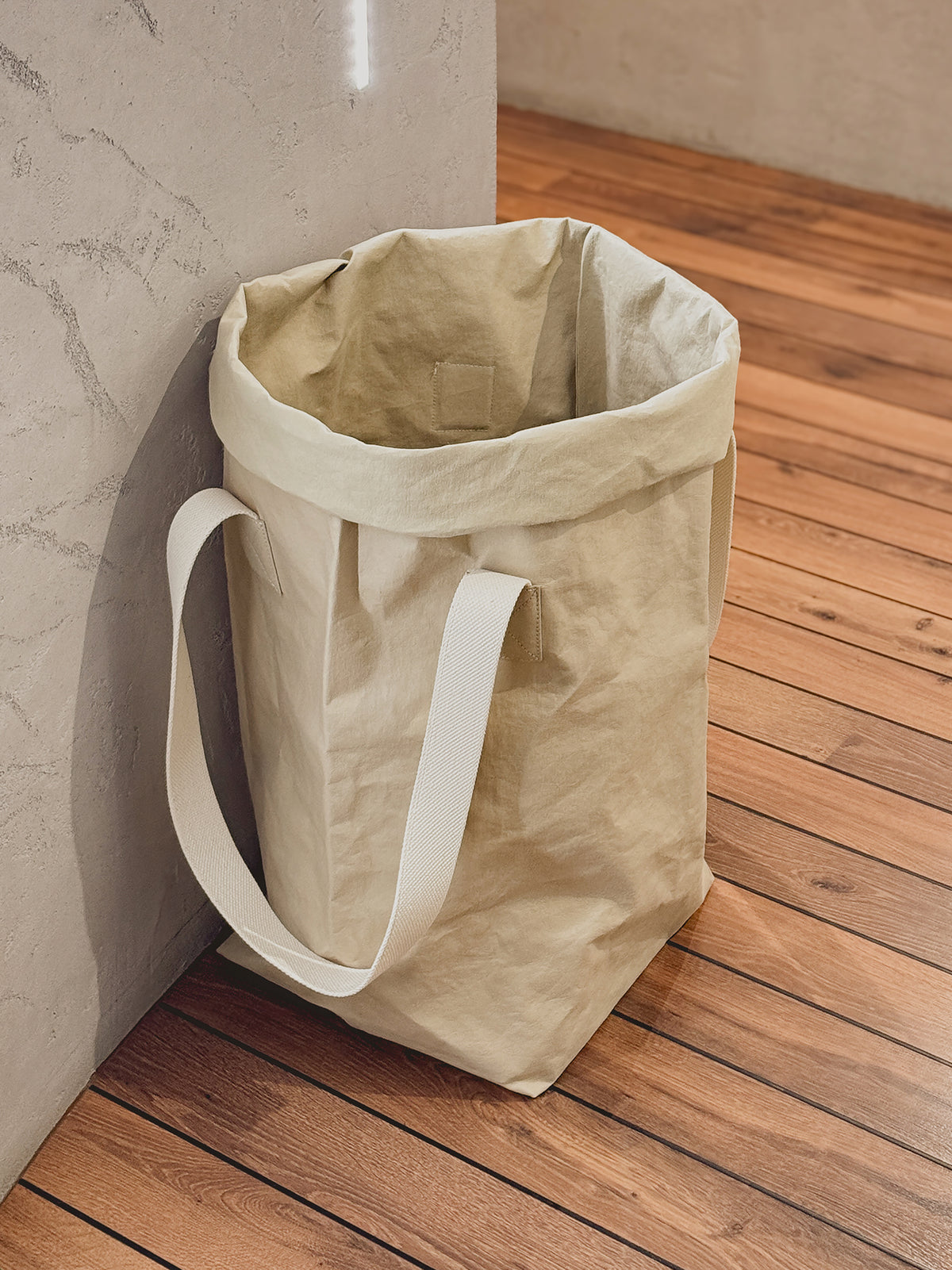 Open sand washable paper laundry basket with natural cotton handles on a wooden floor