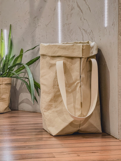 Sand washable paper laundry basket with natural cotton handles next to a potted plant
