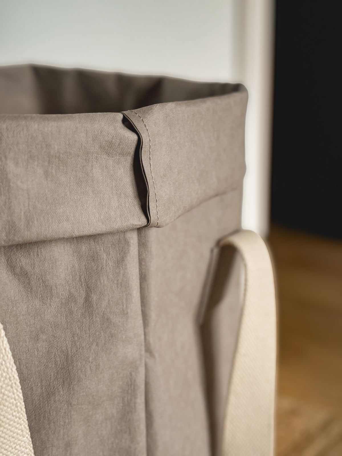 Close-up of the rolled top and natural cotton handle of a grey washable paper laundry basket