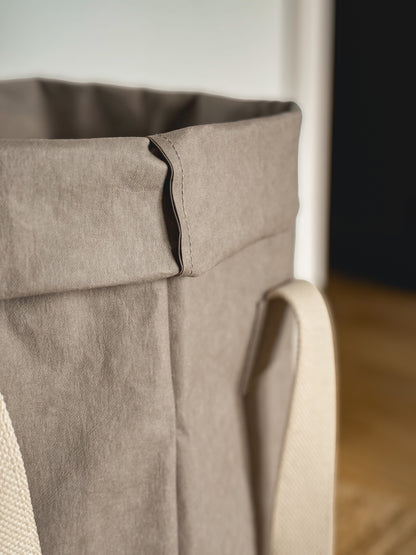 Close-up of the rolled top and natural cotton handle of a grey washable paper laundry basket